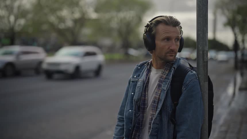 A man leaning against an iron listening to music on headphones