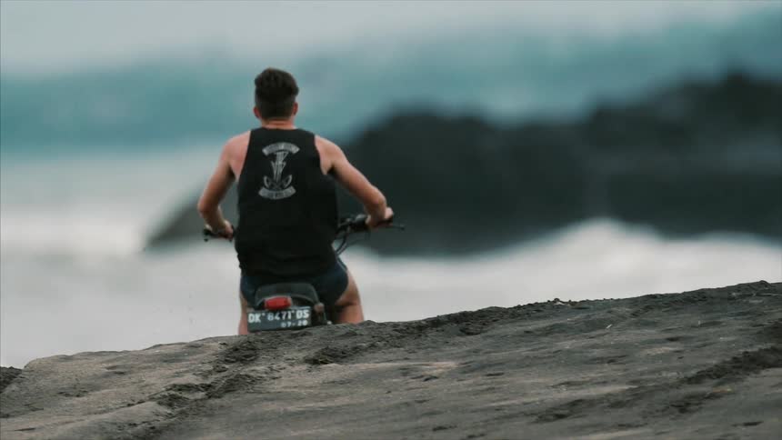 Man rides a dirt bike up a small hill towards the water