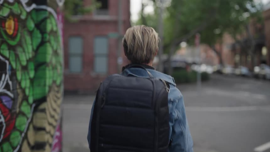 Man in denim jacket with a black backpack walking down the street and turning left