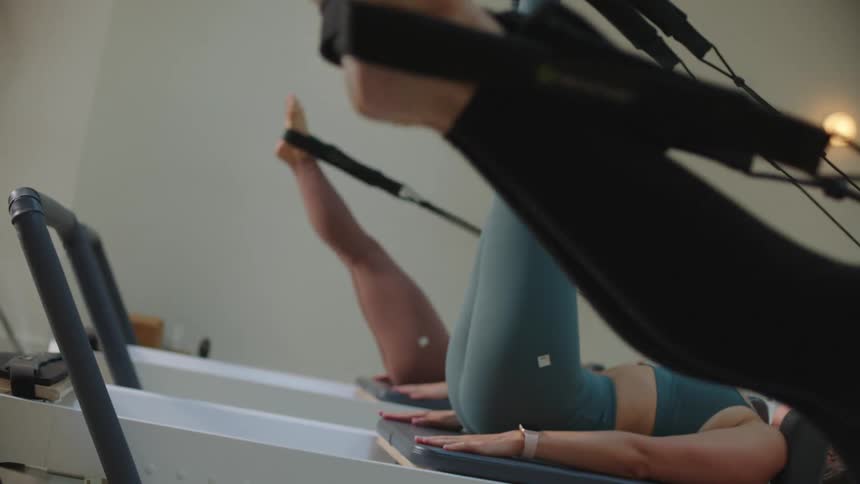 Three women doing pilates lying face up stretching their legs with pilates equipment