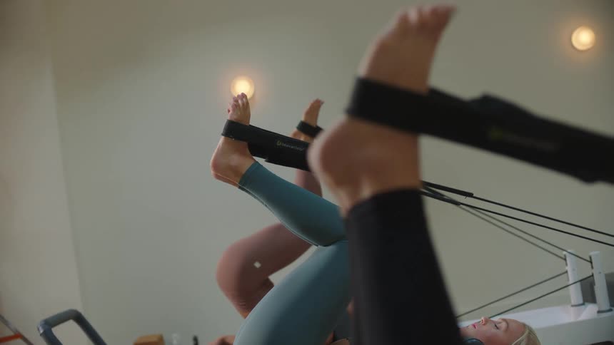 Three women performing leg stretches using elastic bands on a machine