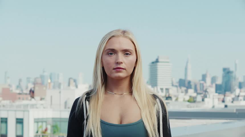 A young blonde woman looking ahead and behind her is a big city