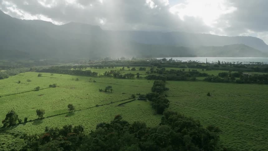 The sun is shining through the clouds on the green field below
