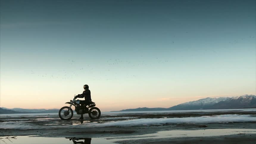 A person sitting on a motorbike in a snow covered area at sunset