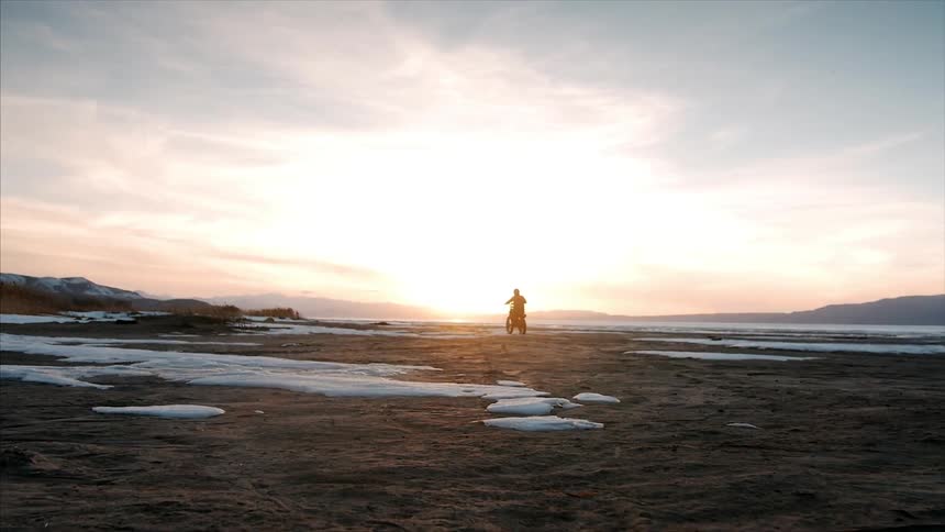 A man is riding his dirt bike across a field at sunset