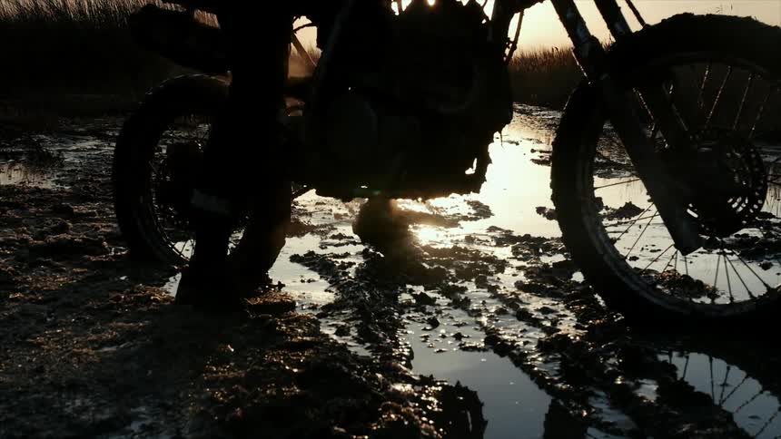 A person sitting on a dirt bike near water at sunset