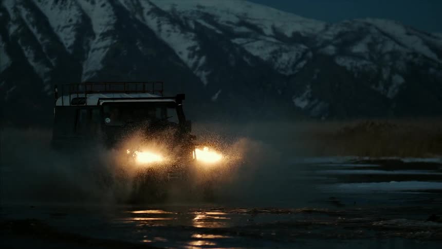 A truck is driving away from a mountain splashing the water on the field