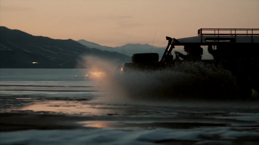 A large suv driving through water at the foot of mountains at night