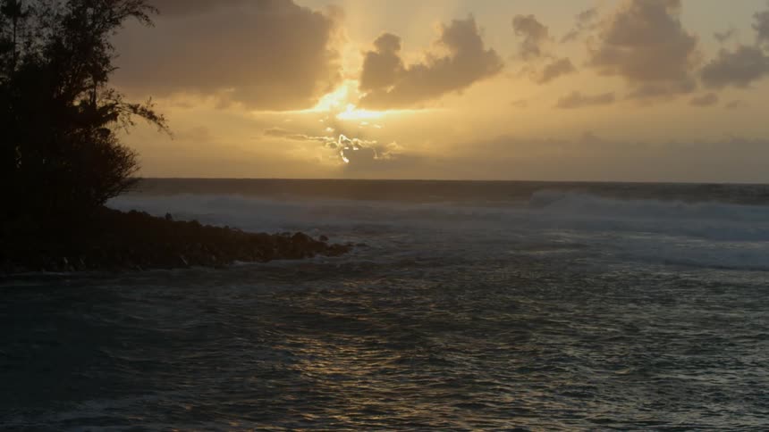 A sunset behind clouds over an ocean with trees