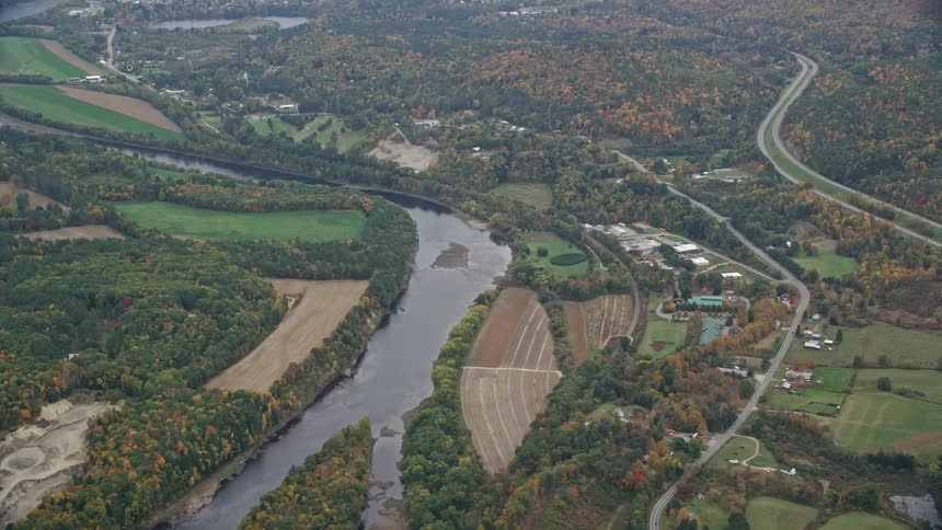 Aerial of river and roads cutting through town surrounded by woods in the autumn