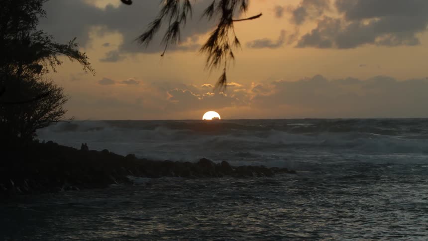 An ocean with the sun setting in the distance and clouds in the sky