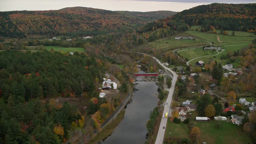 Traffic parallels river through town surrounded by woods in the fall