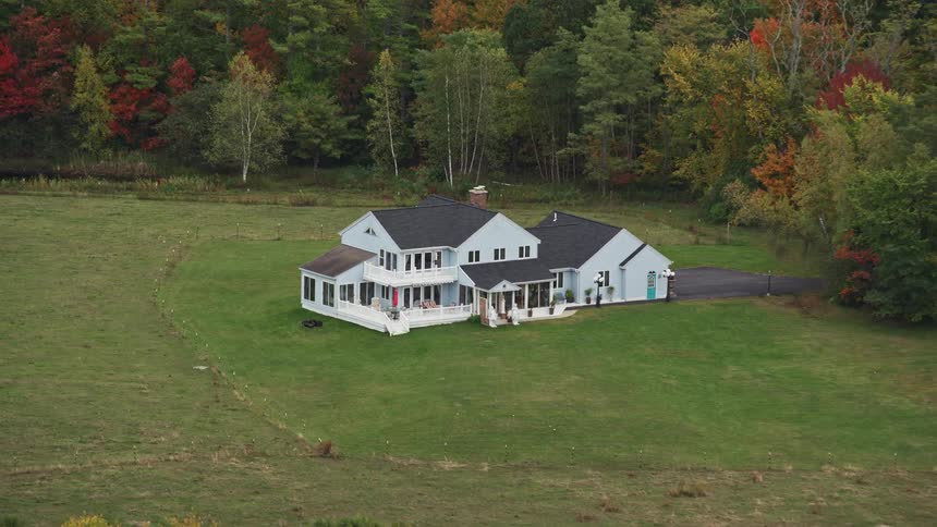 An aerial view of a lawn with just a white house and behind several trees