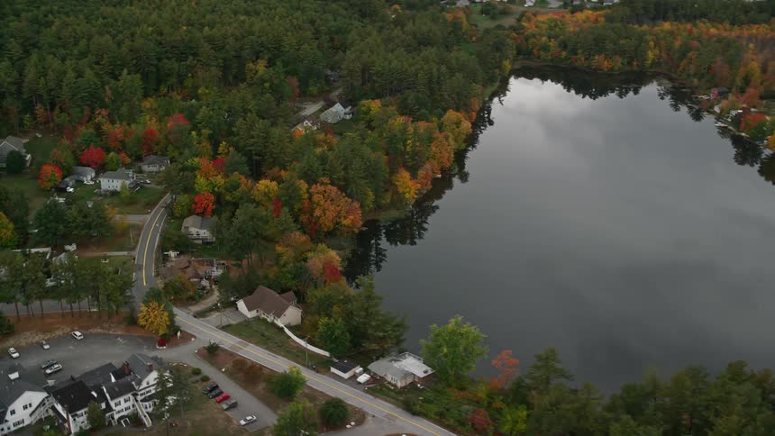 A rural region with some houses facing a lake that reflects the forest trees