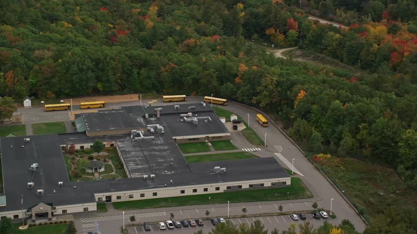 Line of yellow buses drive around campus on cloudy day