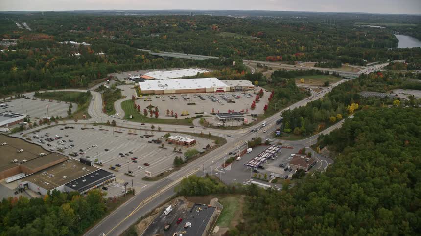 A semirural area with a building with many cars parked next to it and a huge highway with traffic