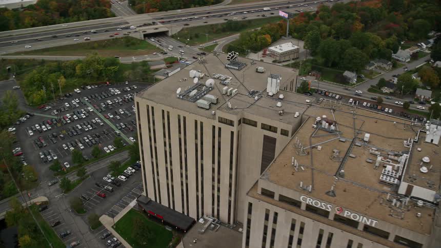 Aerial panorama of an office building in the midst of an urban city with extensive vegetation next to a highway