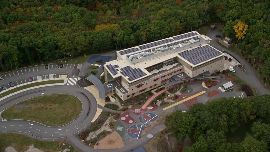 Solar panels cover roof of school building surrounded by woods during the fall