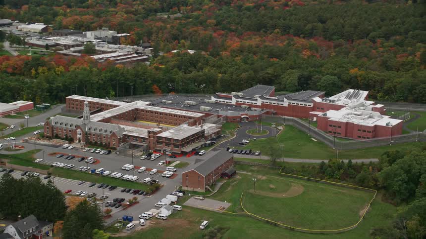 A campus with some buildings and a large parking lot in front and behind a large forest