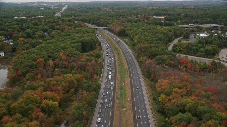 Traffic flows along controlled access highway through town surrounded by woods in fall