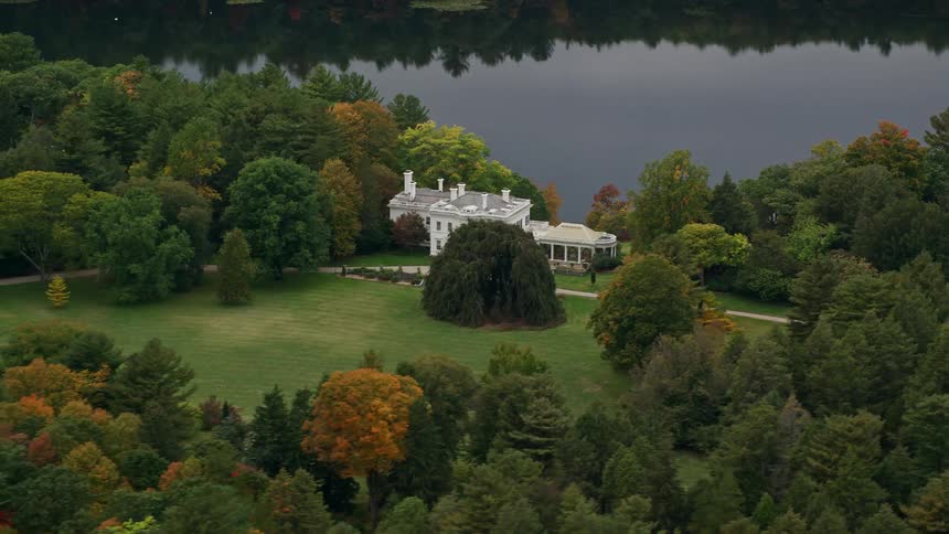 A white mansion surrounded by trees near a lake at midday