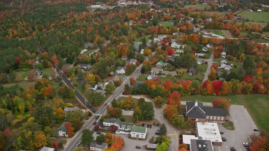 Series of cars moving by a road in a sub urban town filled with residential buildings surrounded by trees