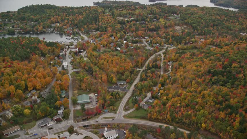 Its a suburban town with buildings scattered around some of them are close to a river and there are boats in a nearby bay the town is surrounded by trees