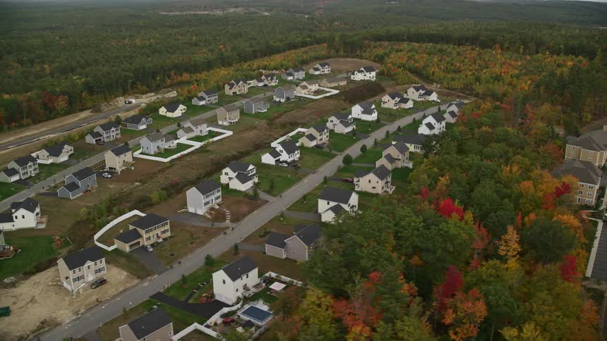 An aerial view of a suburban neighborhood with rows of similarlooking twostory houses featuring a mix of completed and underconstruction homes surrounded by patches of dense autumncolored trees and open land areas