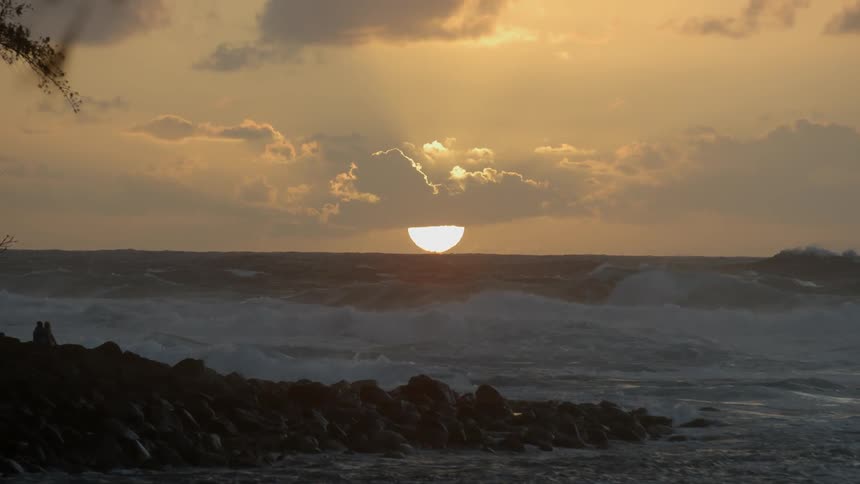 Large waves crash against the shore at sunset