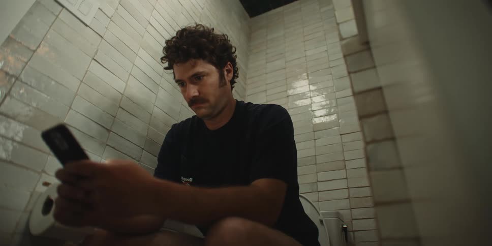Man texts on smartphone while sitting on commode