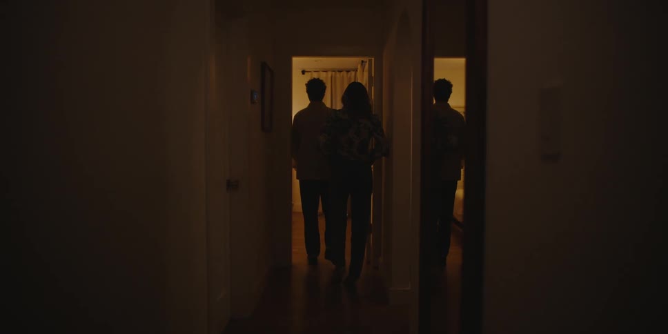 Man and woman walking towards a room in the house at night their backs facing the viewer