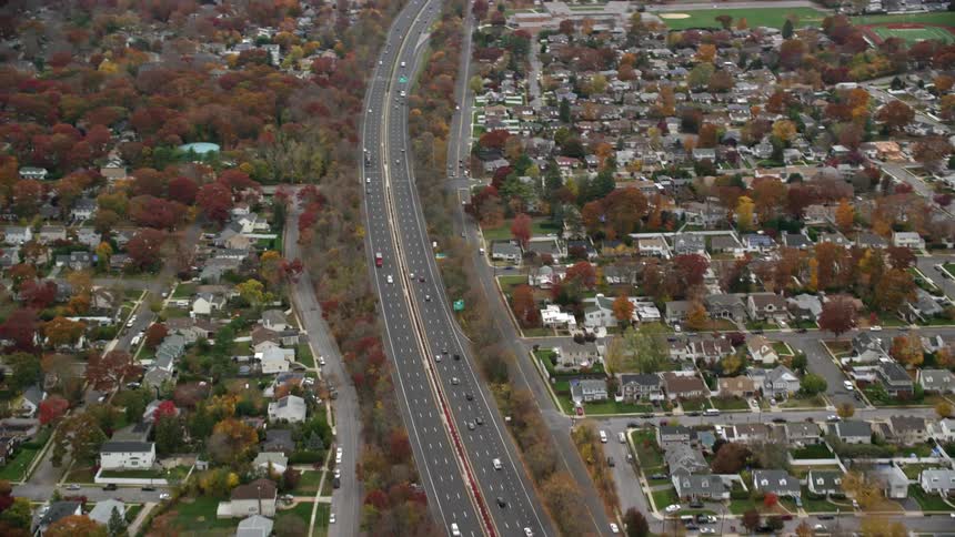 Traffic flows along controlled access highway through residential area during the fall