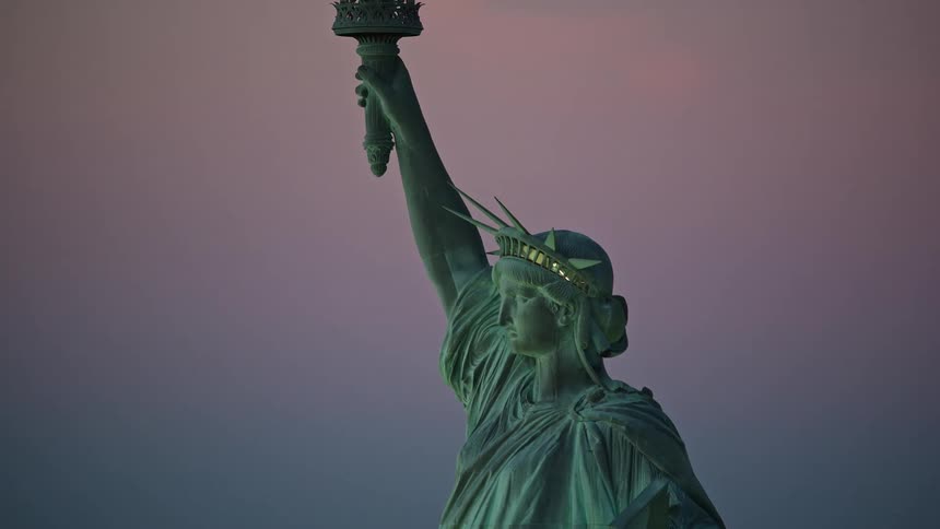 Lights shine out from crown of statue of liberty under a red tinted sky