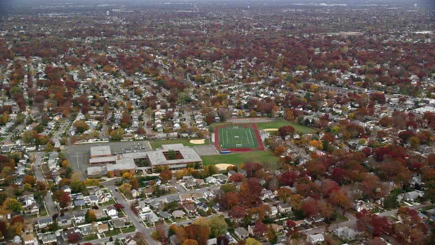Aerial view of sanford h calhoun high school nestled among suburban neighborhoods and trees adorned with autumn leaves and its adjacent sports fields on long island new york