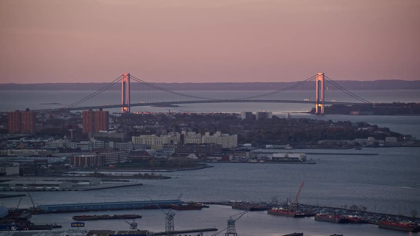 Aerial view of a seaside harbor with the city in the background and a reddish dawn sky
