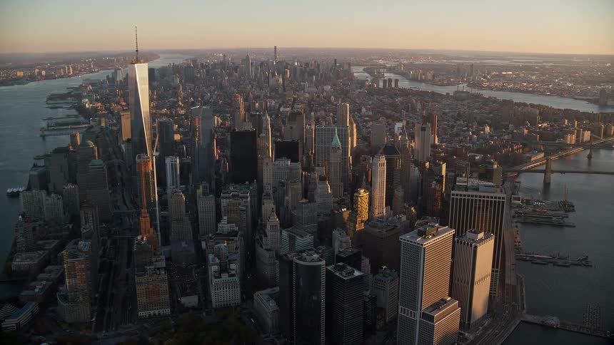 Aerial view of an urban cityscape with dense skyscrapers surrounded by water under the early evening light