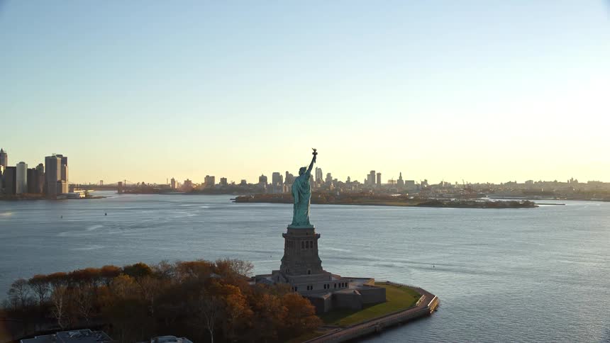 Aerial view captured at sunrise with the statue of liberty in the foreground with a backdrop of the new york city skyline across the water