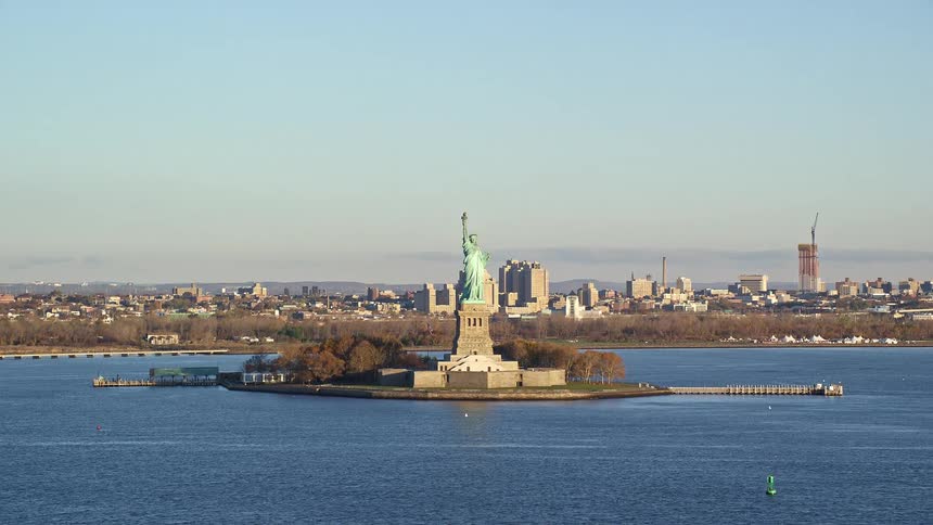 An aerial view of the statue of liberty with its coppergreen patina gleaming in the sunlight on liberty island and the cityscape of manhattan stretches out in the distance