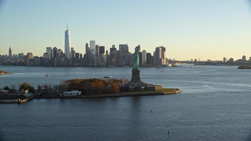 An aerial view of the statue of liberty with its coppergreen patina gleaming in the sunlight on liberty island and the cityscape of manhattan stretches out in the distance