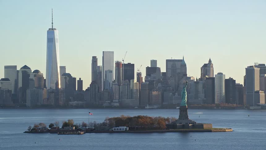 The statue of liberty on an island in the sea and behind the city of new york with tall buildings