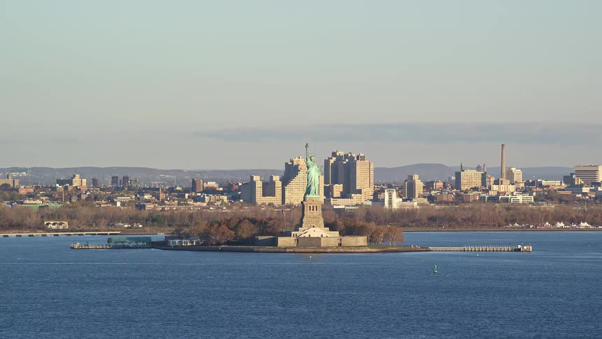Statue of liberty located on the body of water in a metropolitan area at midday