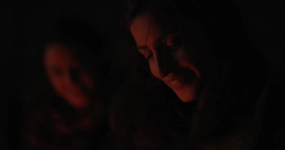 Two women sit by a fire laughing and talking