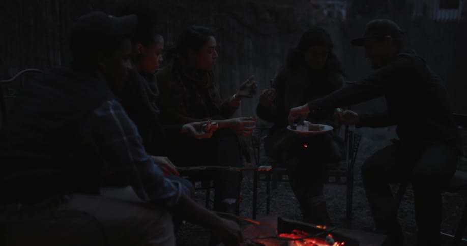 A group of friends sit around a campfire at night