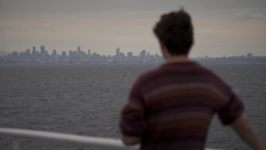 Man with his back to the camera on a boat observing the view on Vancouver in the Sea on the horizon
