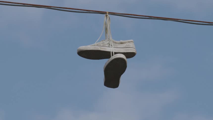 An old sneakers hanging on a wire with its laces in mid day