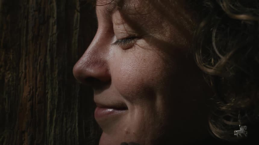 A close up facial clip of a lady smiling while hugging a tree