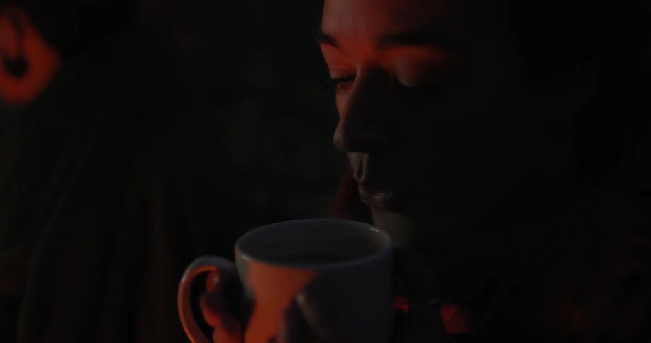 A woman drinks from a mug in the dark