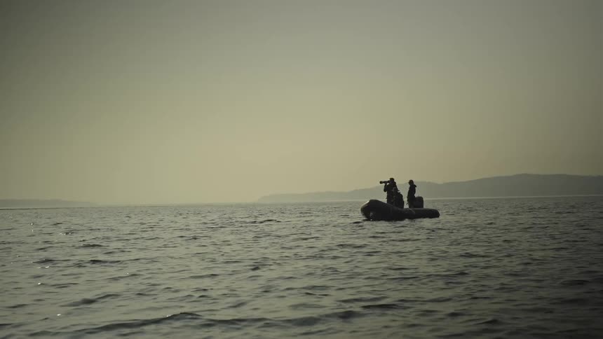 A silhouette of some people in a small canoe in the sea and one person is wearing monoculars