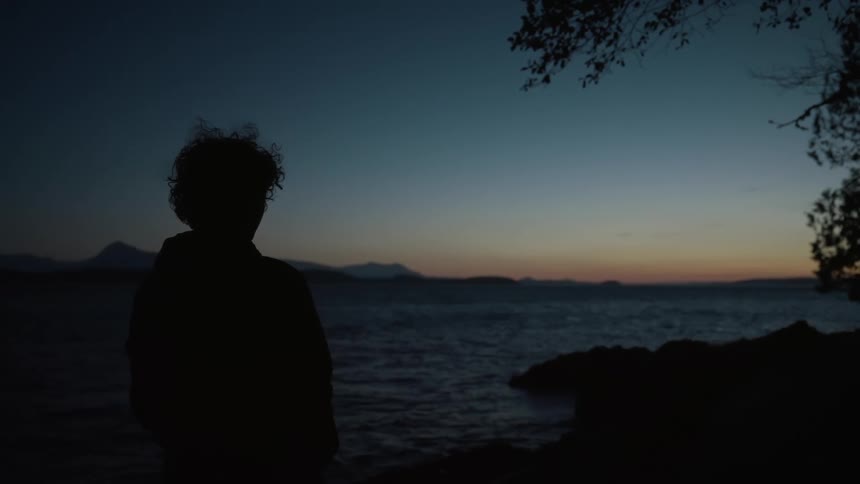 Back view of someone standing near a river at sunset