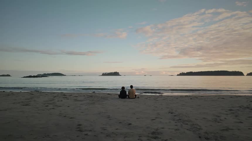 A couple sitting on the beach sand on a morning